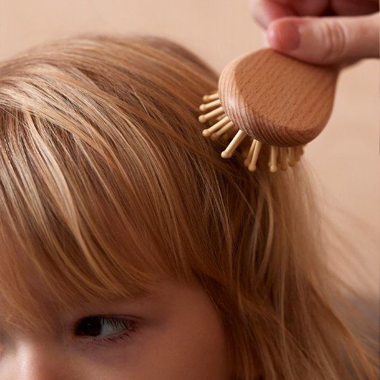 Brosse cheveux bébé a picots en bois utilisee sur les cheveux blonds d un enfant