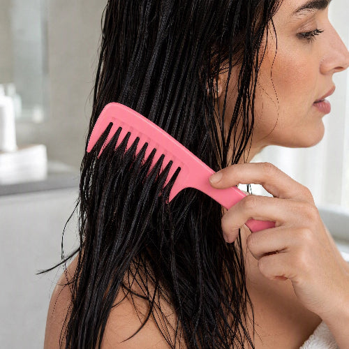 Peigne femme rose a dents larges sur cheveux longs mouilles vus de profil en gros plan