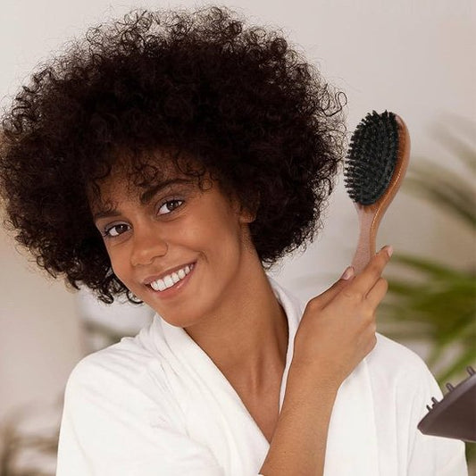 Brosse-à-cheveux-en-poil-de-sanglier-coiffant-chevelure-bouclee-dans-piece-claire-avec-plante