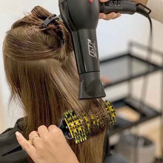 Brushing-avec-brosse-à-cheveux-bouclés-ronde-lissant-meche-brune-dans-salon-de-coiffure