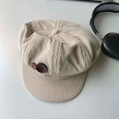 Casquette-gavroche-beige-en-velours-côtelé-avec-bouton-marron-posée-sur-une-surface-blanche
