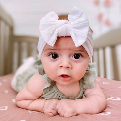 bebe-allonge-regard-curieux-bandeau-cheveux-bebe-noeud-blanc-tenue-verte-douceur-lit