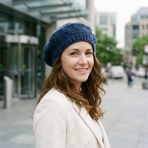 Béret bleu marine en chenille porte par une femme en blazer creme devant un batiment de bureaux