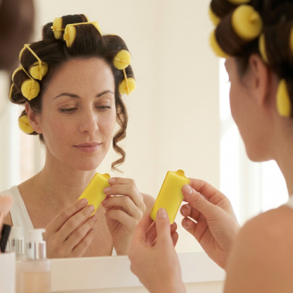 Bigoudis mousse femme devant le miroir tenant un bigoudi jaune