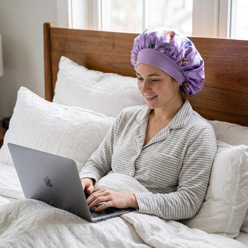 Bonnet en satin cheveux violet femme travaille avec son ordinateur sur son lit