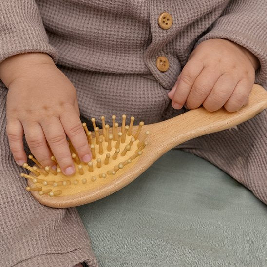 Brosse cheveux bébé a picots en bois tenue par un bebe en tenue maillee