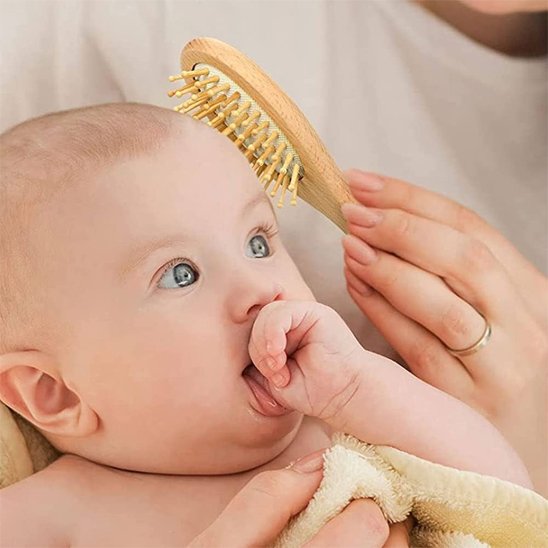Brosse cheveux bébé en bois passant sur la tete d un bebe qui suce son pouce