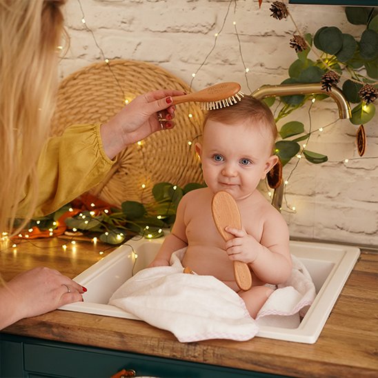 Brosse cheveux bébé en bois utilisee sur un bebe assis tenant une seconde brosse