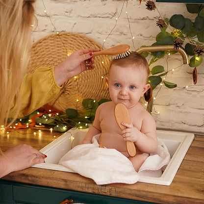 Brosse cheveux bébé en bois utilisee sur un bebe assis tenant une seconde brosse