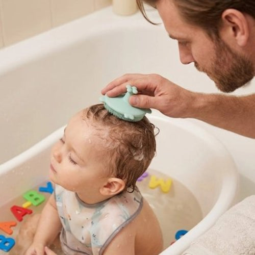 Brosse cheveux bébé verte utilisee par un homme pendant le bain avec des jouets colores