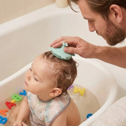 Brosse cheveux bébé verte utilisee par un homme pendant le bain avec des jouets colores