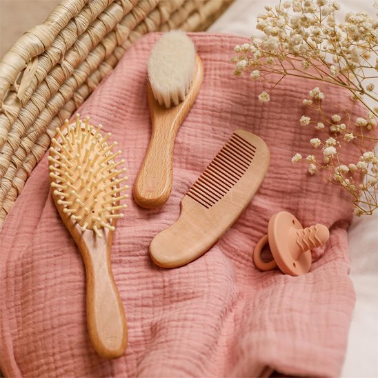 Brosse cheveux pour bébé en bois avec une seconde brosse et un peigne sur un tissu rose