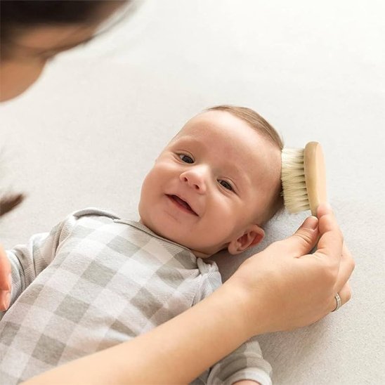 Brosse cheveux pour bébé en bois passant sur le cote de la tete du nourrisson souriant