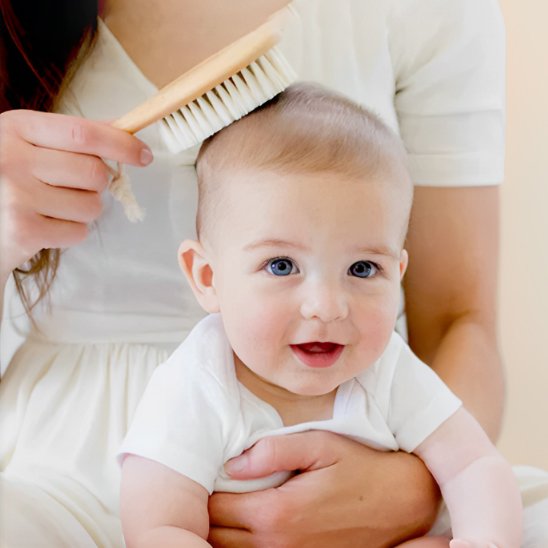 Brosse cheveux pour bébé en bois utilisee sur la tete du tout petit tenu dans les bras