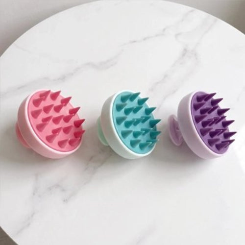 Brosse massage cuir chevelu​ rose turquoise et violette posees cote a cote sur une surface claire