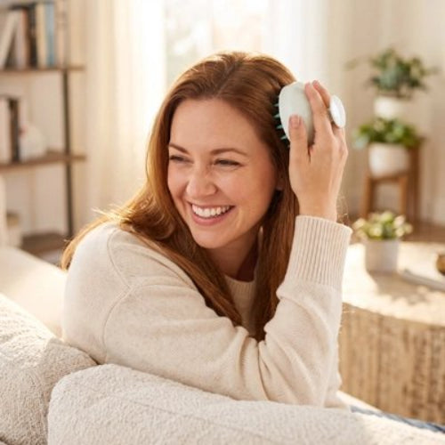 Brosse massage cuir chevelu​ tenue sur le dessus de la tete par une femme souriante en pull clair