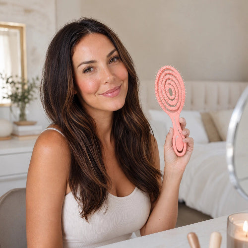 Brosse pour cheveux boucles rose tenue par une femme aux cheveux longs