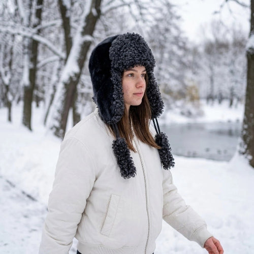 Chapka femme gris anthracite avec pompons portee avec une veste blanche en foret enneigee