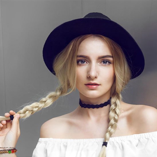 Élastiques cheveux noirs au bout de deux tresses blondes sur une femme portant un chapeau