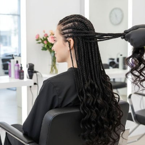 Extension de cheveux noirs en cours de pose sur des tresses dans un salon de coiffure