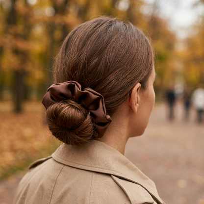 Grand chouchou cheveux soie cafe brun porte autour d un chignon bas par une femme en manteau beige dans un parc