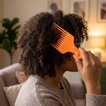 Peigne à dents larges orange utilise par une femme vue de profil sur ses cheveux boucles dans un salon