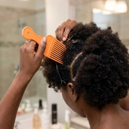 Peigne à dents larges orange utilise sur des cheveux afro separes en sections dans une salle de bain