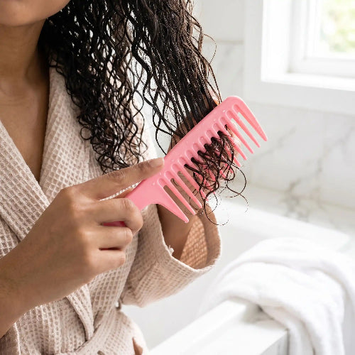 Peigne grande dent rose utilise par une femme en peignoir beige pour demeler ses cheveux boucles mouilles