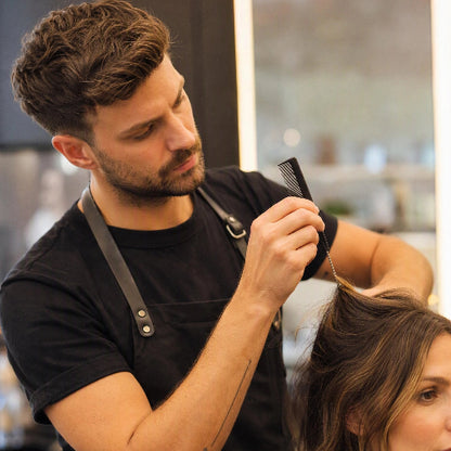 Peigne noir a queue metallique utilise par un coiffeur pour soulever une meche de cheveux