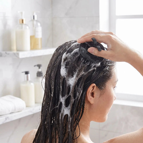 Peigne noir masseur utilise par une femme sur ses cheveux mouilles avec de la mousse de shampooing