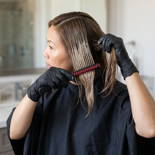Peigne professionnel noir rouge utilise par une femme asiatique portant des gants pour repartir elle meme sa coloration sur une meche