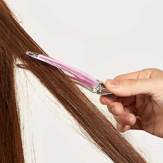 Pinces à cheveux crocodile pince rose tenue a la main sur une meche de cheveux bruns