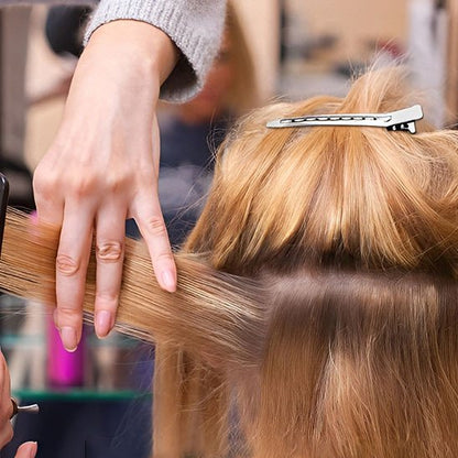 Pinces crocodiles argentees pour maintenir une section de cheveux blonds pendant la coupe