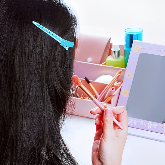 Pinces crocodiles turquoise sur cheveux noirs pendant le maquillage devant un miroir