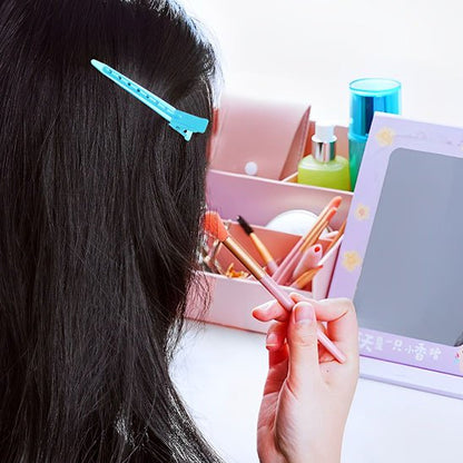 Pinces crocodiles turquoise sur cheveux noirs pendant le maquillage devant un miroir