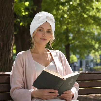 Turban pour femme blanc avec noeud sur le devant porte par une femme avec un livre sur un banc