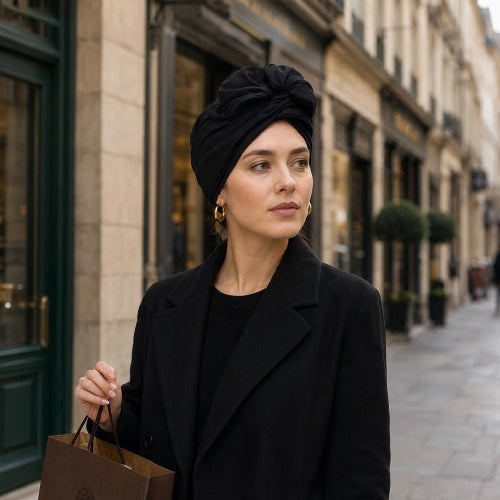 Turban pour femme noir avec noeud sur le devant porte avec un manteau noir dans une rue