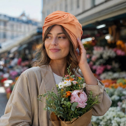 Turban pour femme orange peche avec noeud sur le devant porte par une femme tenant un bouquet de fleurs